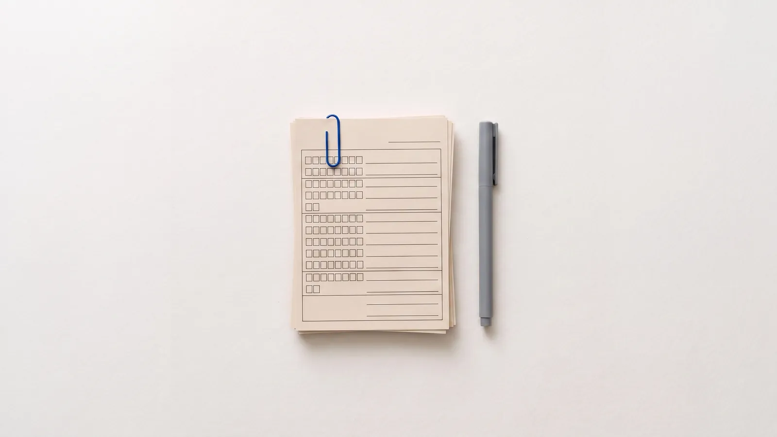 A clipped stack of blank printed forms next to a pen