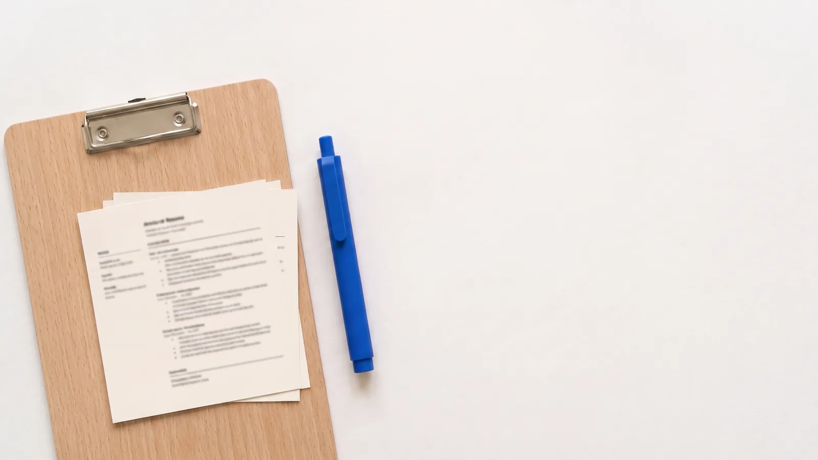 Printed CVs on a clipboard next to a pen